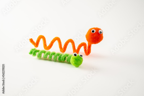 googly eyed pom pom pipe cleaner orange wriggly worm green caterpillar funny character childs toy hand made isolated on a white background photo