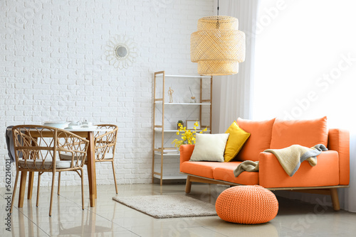 Stylish interior of living room with orange sofa, pouf and dining table