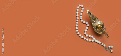 Aladdin lamp of wishes and prayer beads on orange background with space for text