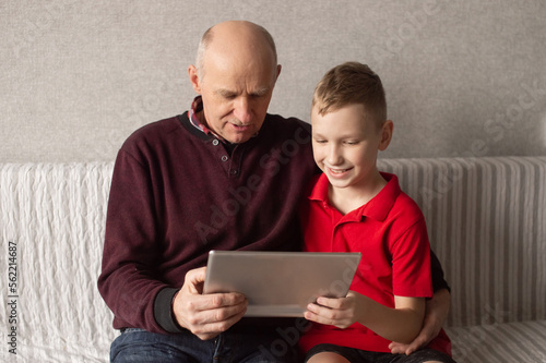 Happy grandfather and grandson look into the gadget and hug