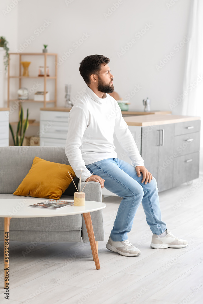 Thoughtful young bearded man sitting on sofa in kitchen Thoughtful young bearded man sitting on sofa in kitchen