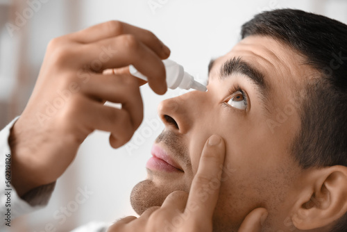 Young man using eye drops a...