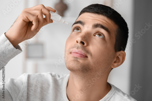 Young man using eye drops a...