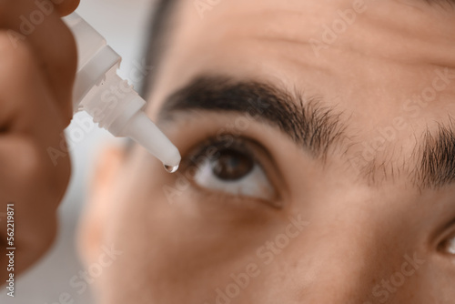 Young man using eye drops a...