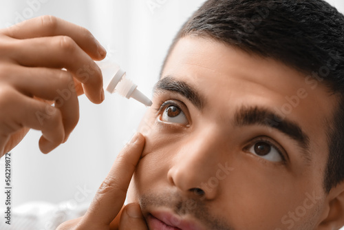 Young man using eye drops a...