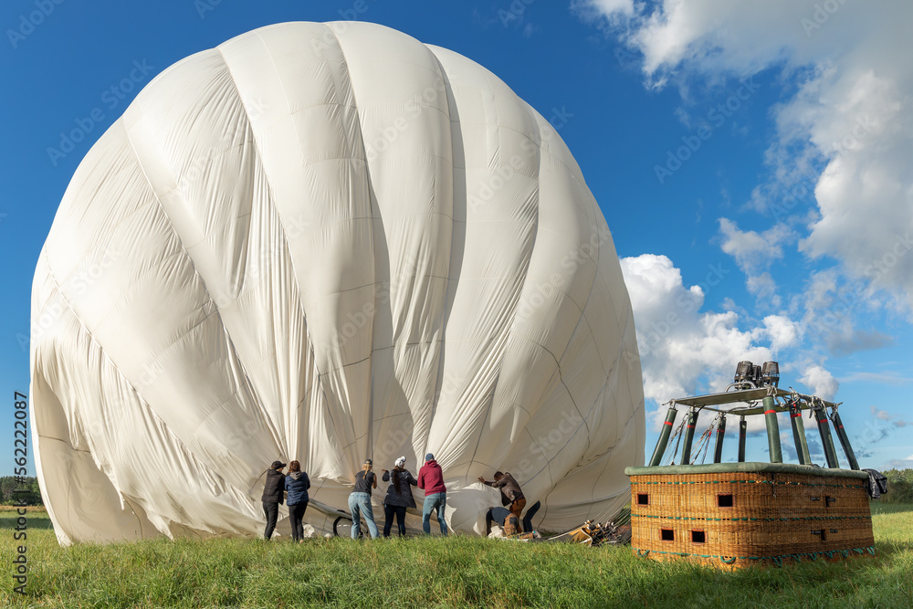 Obraz premium The hot air balloon and the team after the flight. People all together help to release the remaining air from the balloon and prepare it for transportation