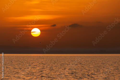 Fototapeta Naklejka Na Ścianę i Meble -  Sunset above a lake, with sharp sun and small clouds