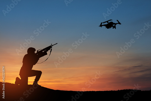 Soldier trying to shoot down reconnaissance drone against the backdrop of a sunset. Soldier shoots a quadcopter. Modern methods of warfare. Technology concept.