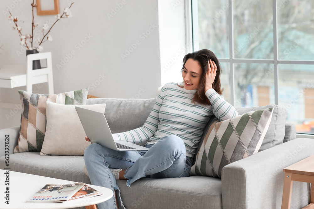 Young woman using laptop on grey couch in living room Young woman using laptop on grey couch in living room