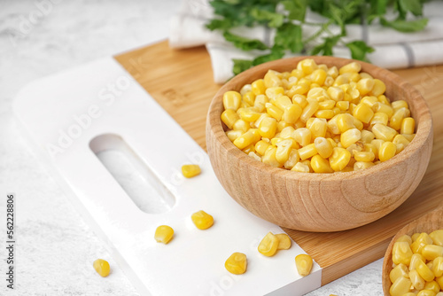 Cutting board with spoon and bowl of canned corn kernels on white table