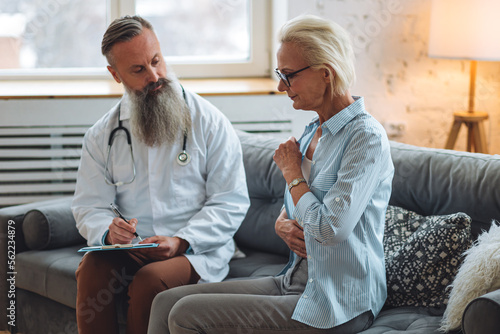 Male doctor visiting attractive senior woman at home for consultation, medical service and support, geriatric help, prescribing illness treatment. Clinic or hospital appointment, cancer recovery