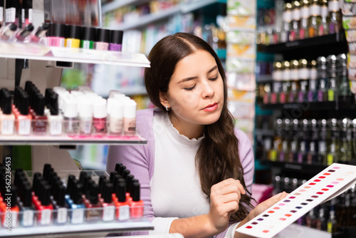 Portrait of attractive young girl choosing nail polish from color samples in makeup store