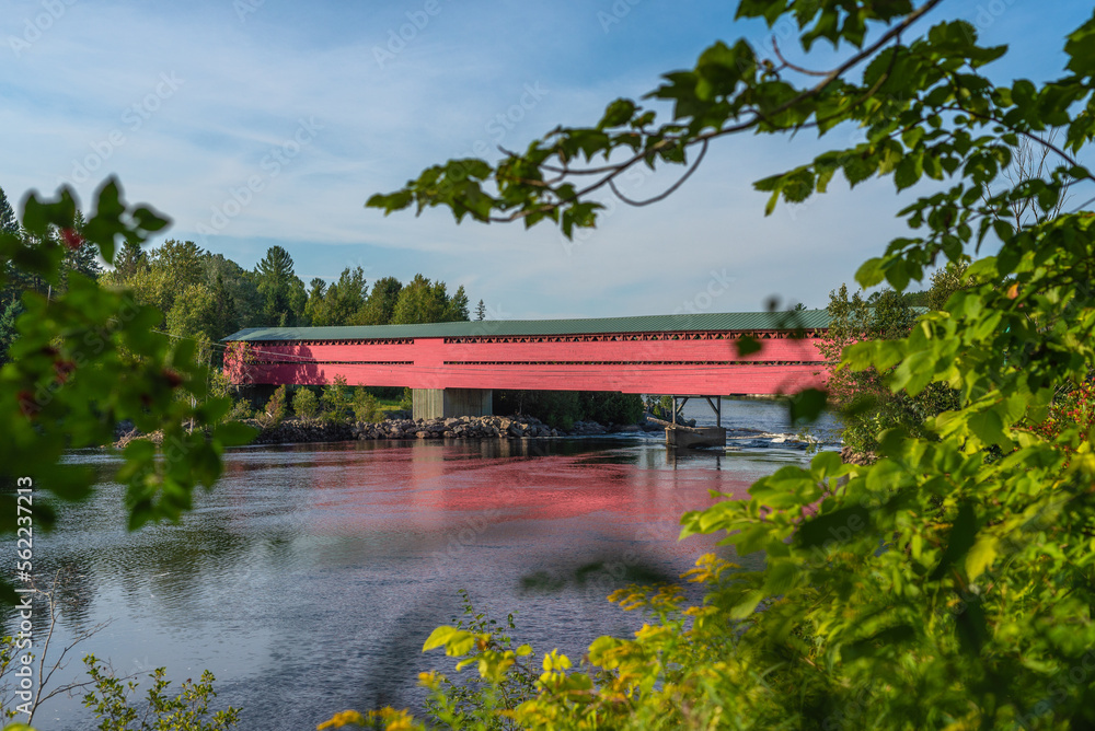A red wooden covered bridge over a large river in Quebec, Canada A red wooden covered bridge over a large river in Quebec, Canada