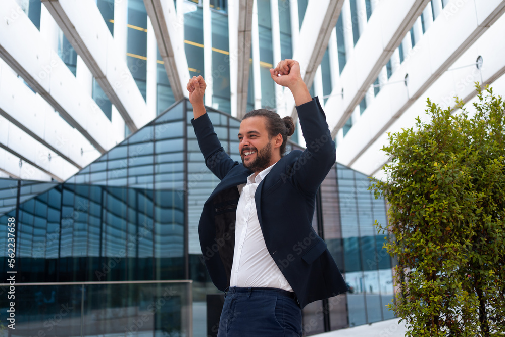 Excited young businessman in suit celebrating victory arms raised
