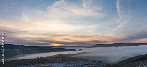 Winter panorama at sunset with snow covered hills with low fog in the valley and cloud cover  hills with snow and trees in winter at sunset