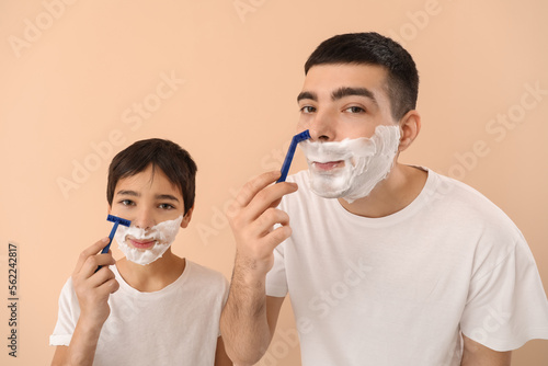 Father and his little son shaving against beige background