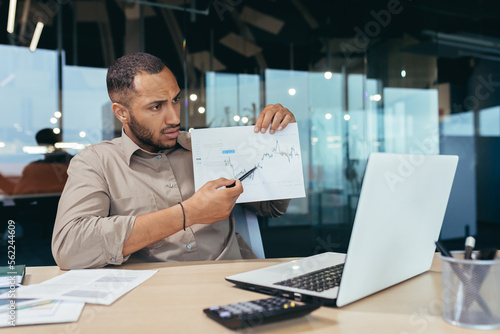 Dissatisfied businessman shows a graph with bad achievements to the camera on a video call, a Latin American man reports negative results at an online meeting of company managers, a man at work.