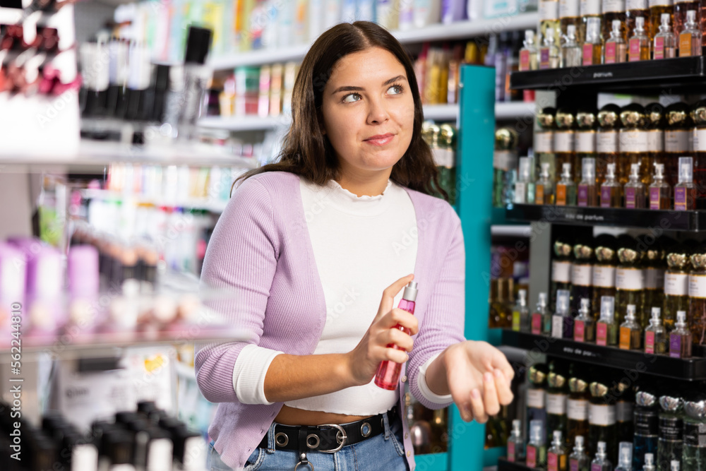 Satisfied young woman chooses and tries perfume in a cosmetics store