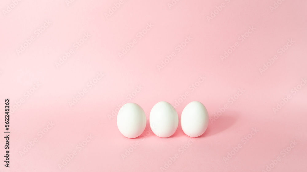 Three white chicken eggs isolated on light pink pastel background. Happy Easter Day.