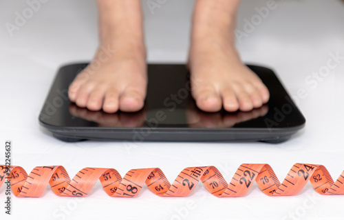 A Body Measuring Tape or Soft Measuring Tape Ruler with a person on a scale on the background. Concept: Weight loss