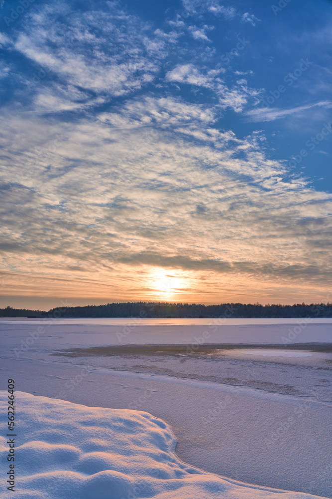 Sunset clouds over frozen lake. Sunset colors reflection in snow covered lake. Frozen lake pier on sunset