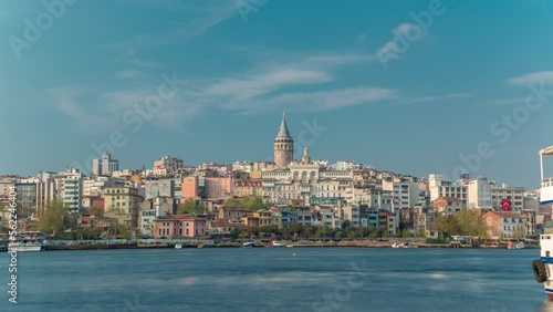 Beyoglu district historic architecture and Galata tower medieval landmark timelapse in Istanbul, Turkey. Many colorful houses reflected in water. Blue cloudy sky at spring sunny day photo