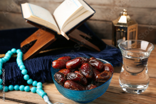 Bowl with dried dates and glass of water for Ramadan on wooden table, closeup photo