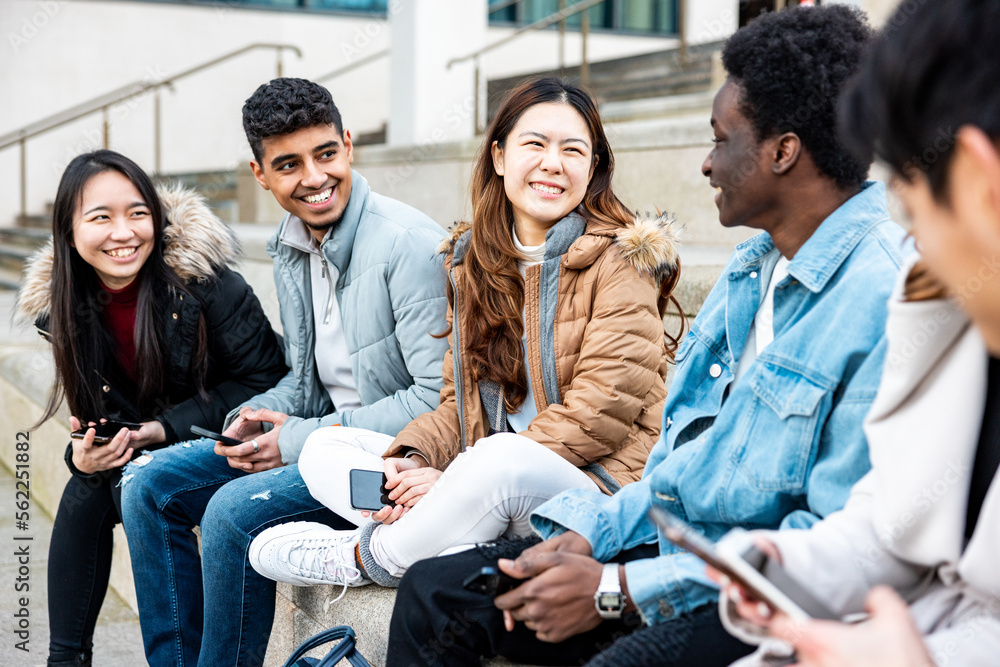 Happy group of friends in the city using mobile phones and laughing together