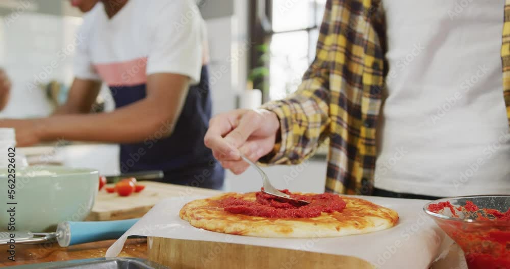 Happy diverse male teenage friends preparing pizza in kitchen, slow motion Happy diverse male teenage friends preparing pizza in kitchen, slow motion