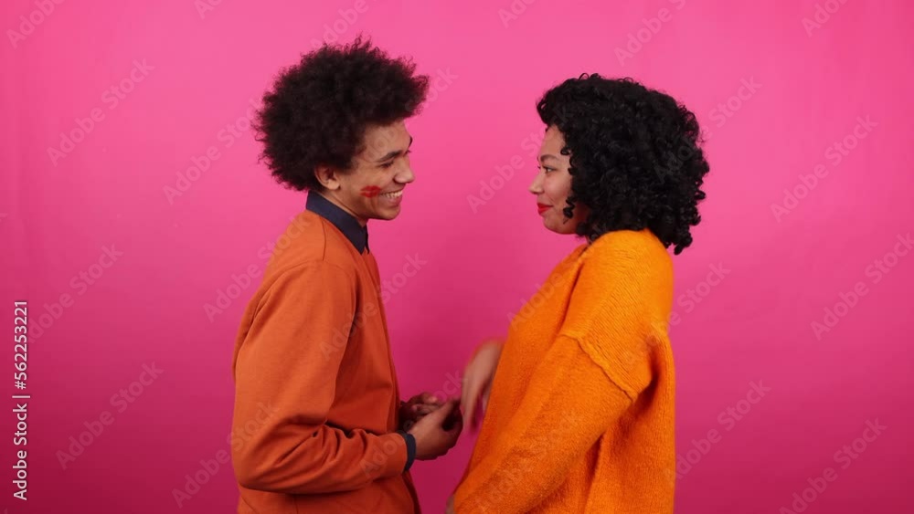 Portrait of a woman kissing her boyfriend with pink isolated background behind. Girlfriend leaving lipstick mark on the face of a guy. High quality 4k footage Portrait of a woman kissing her boyfriend with pink isolated background behind. Girlfriend leaving lipstick mark on the face of a guy. High quality 4k footage