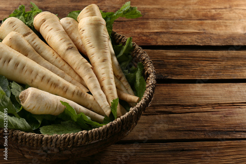 Fresh ripe parsnips in wicker basket on wooden table. Space for text photo