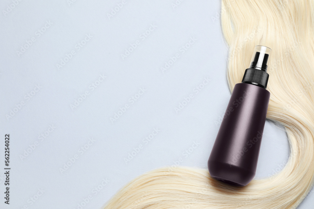 Fototapeta premium Spray bottle with thermal protection and lock of blonde hair on light background, flat lay. Space for text