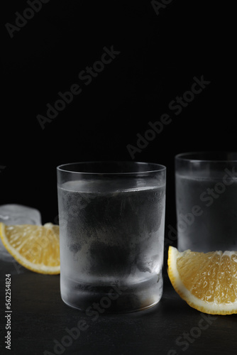 Shot glasses of vodka with lemon slices and ice on black background