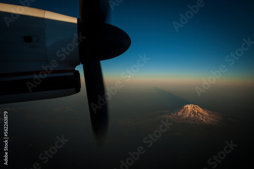 A snow capped mountain seen at sunset through an airplane window with the propeller as a frame. photo