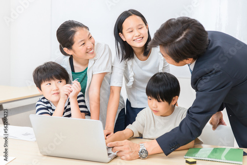 学校の授業でパソコンを使って勉強する小学生の子供達と先生（ICT教育・学校・塾・クラスメイト）