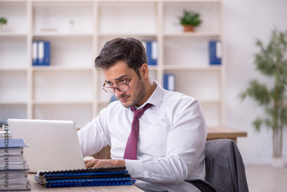 Young male employee and too much work at workplace Young male employee and too much work at workplace