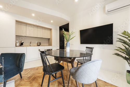Loft with glass round black dining table with vase and open plan kitchen in contemporary design  wall mounted tv and assorted chairs with varnished oak flooring