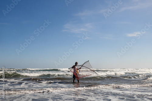 A fisherman who is looking for fish on the shore using a net