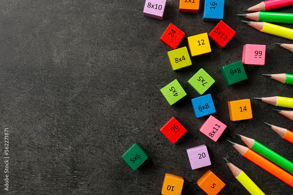 Obraz premium Many colorful cubes with numbers, multiplications and pencils on dark grey table, flat lay. Space for text