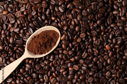 Spoon with ground coffee on roasted beans, top view. Space for text