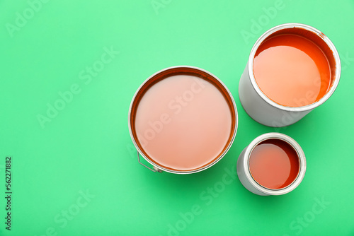 Cans of orange paint on green background, top view. Space for text