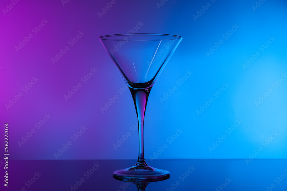 Empty clean martini glass on mirror table in neon lights Empty clean martini glass on mirror table in neon lights