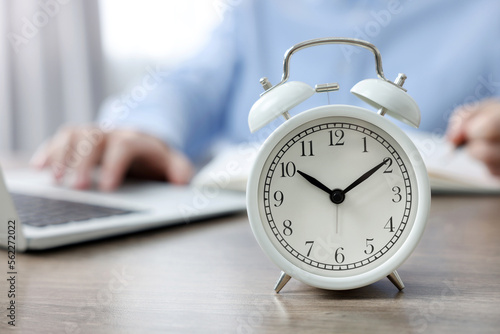 White alarm clock and man working at table, closeup. Space for text