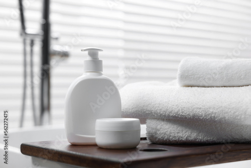 Stacked bath towels and personal care products on tub tray in bathroom, closeup