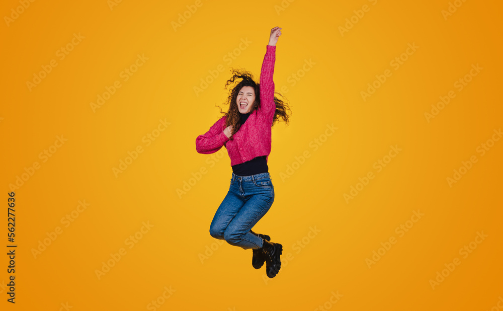 Cheerful funny young woman in casual clothes jumping and spreading hands isolated on yellow wall background in studio. People sincere emotions, lifestyle