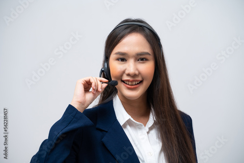Beautiful Asian call center operator talking with customer using headset and microphone isolated on grey background.