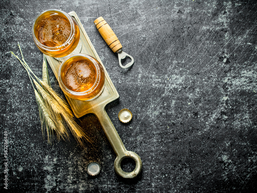 Two glasses of beer on a stand with spikelets and opener.