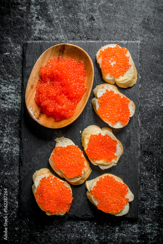 Red caviar in a bowl and caviar sandwiches on a black stone Board.
