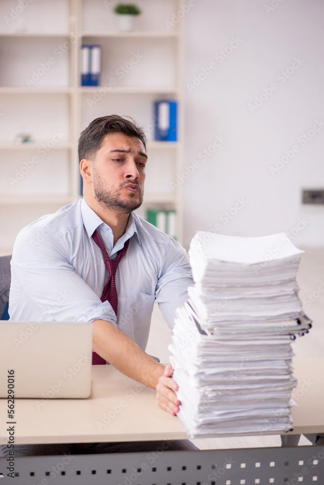 Young male employee unhappy with excessive work in the office Young male employee unhappy with excessive work in the office