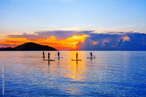 People silhouettes stand SUP paddle boarding, sea sunset beach, active young man woman surfing paddling board, ocean sunrise, surfboard, healthy lifestyle, water sport, summer holidays, relax vacation photo